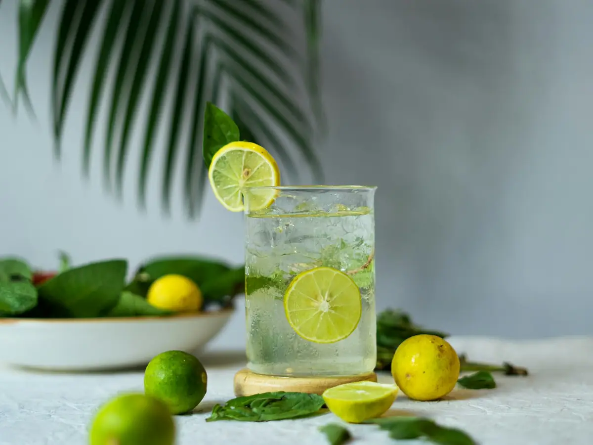 Segelas minuman sari lemon dingin dengan buah lemon dan jeruk nipis segar